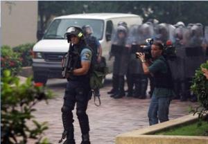 A news camera man films SWAT police as they persue students through the University of Puerto Rico in Rio Piedras. One officer stands ready with a bean bag guns. 